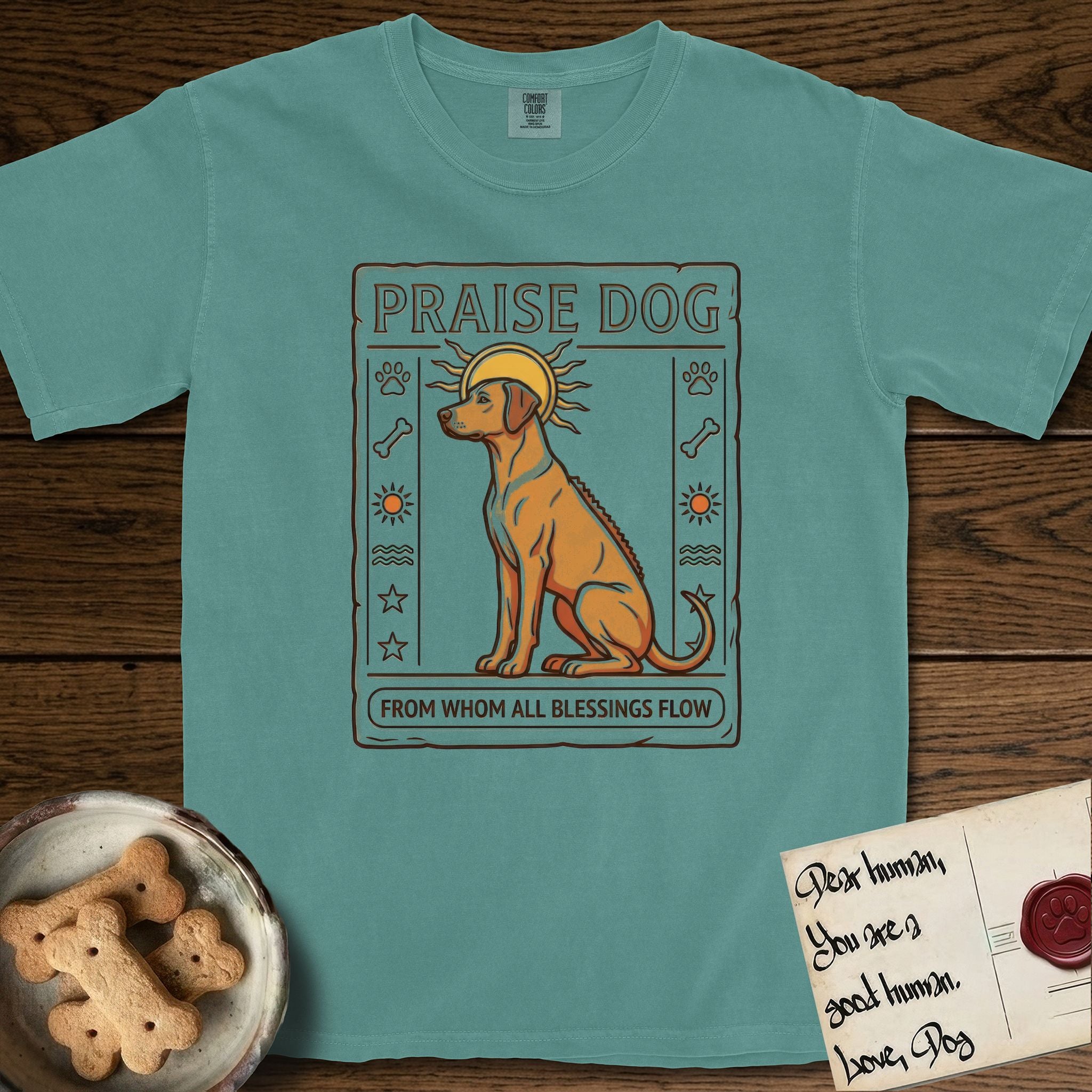 Praise Dog From Whom All Blessings Flow Rhodesian Ridgeback T-Shirt flat lay in Blue Spruce, featuring an ancient Egyptian carved-relief emblem of a Rhodesian Ridgeback in side profile with a visible spine ridge, a rayed golden sun halo, hieroglyph glyph columns, and a ragged stone border with "Praise Dog From Whom All Blessings Flow" lettering.