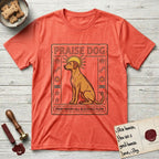 Praise Dog From Whom All Blessings Flow Rhodesian Ridgeback T-Shirt flat lay in Heather Orange, featuring an ancient Egyptian carved-relief emblem of a Rhodesian Ridgeback in side profile with a visible spine ridge, a rayed golden sun halo, hieroglyph glyph columns, and a ragged stone border with "Praise Dog From Whom All Blessings Flow" lettering.