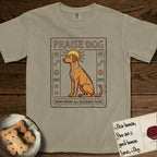 Praise Dog From Whom All Blessings Flow Rhodesian Ridgeback T-Shirt flat lay in Khaki, featuring an ancient Egyptian carved-relief emblem of a Rhodesian Ridgeback in side profile with a visible spine ridge, a rayed golden sun halo, hieroglyph glyph columns, and a ragged stone border with "Praise Dog From Whom All Blessings Flow" lettering.