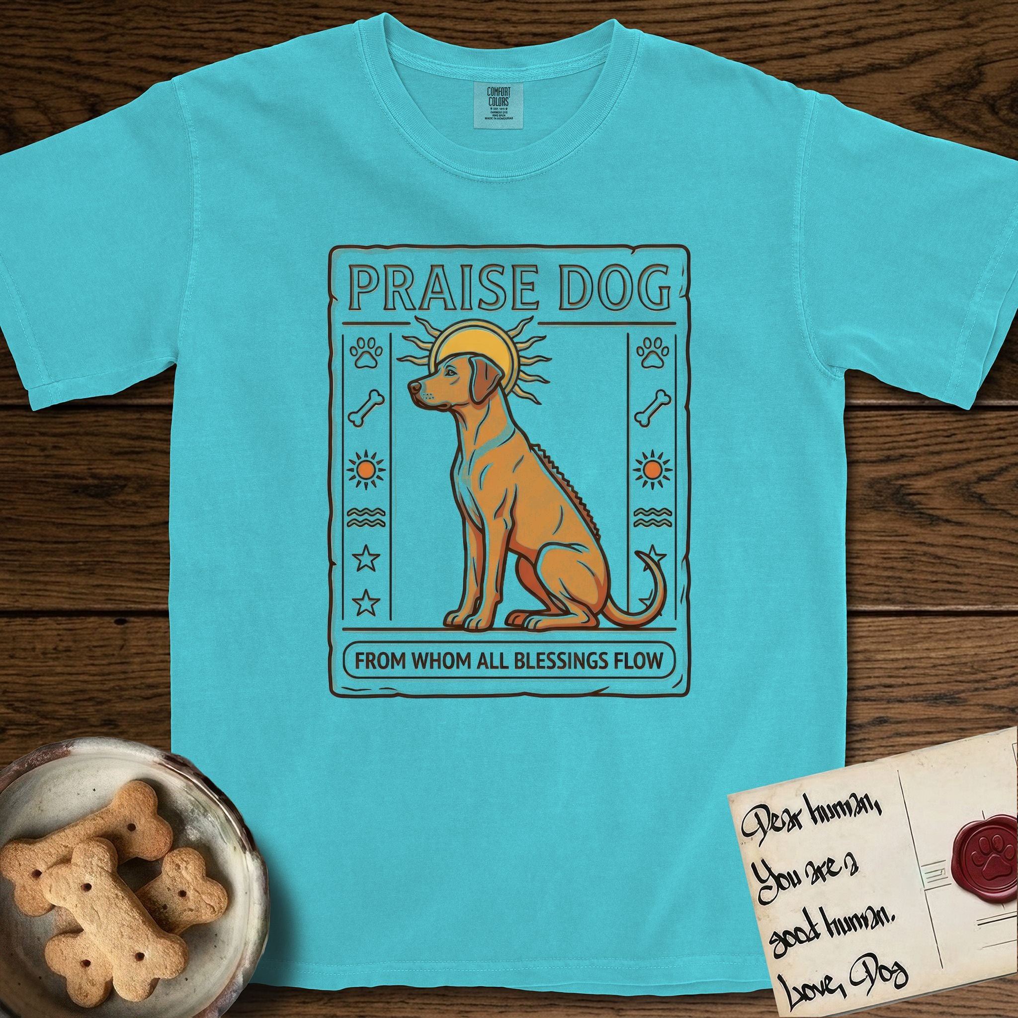 Praise Dog From Whom All Blessings Flow Rhodesian Ridgeback T-Shirt flat lay in Lagoon Blue, featuring an ancient Egyptian carved-relief emblem of a Rhodesian Ridgeback in side profile with a visible spine ridge, a rayed golden sun halo, hieroglyph glyph columns, and a ragged stone border with "Praise Dog From Whom All Blessings Flow" lettering.
