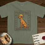 Praise Dog From Whom All Blessings Flow Rhodesian Ridgeback T-Shirt flat lay in Sage, featuring an ancient Egyptian carved-relief emblem of a Rhodesian Ridgeback in side profile with a visible spine ridge, a rayed golden sun halo, hieroglyph glyph columns, and a ragged stone border with "Praise Dog From Whom All Blessings Flow" lettering.