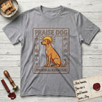 Praise Dog From Whom All Blessings Flow Rhodesian Ridgeback T-Shirt flat lay in Sport Grey, featuring an ancient Egyptian carved-relief emblem of a Rhodesian Ridgeback in side profile with a visible spine ridge, a rayed golden sun halo, hieroglyph glyph columns, and a ragged stone border with "Praise Dog From Whom All Blessings Flow" lettering.