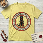 Praise Dog From Whom All Blessings Flow Rottweiler T-Shirt flat lay in Cornsilk, featuring a Roman mosaic ring medallion of a seated Rottweiler with natural ears and a full undocked tail, built from terracotta and mahogany tiles and flanked by laurel branches, with "Praise Dog From Whom All Blessings Flow" lettering.