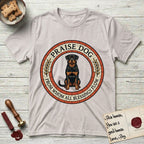 Praise Dog From Whom All Blessings Flow Rottweiler T-Shirt flat lay in Ice Grey, featuring a Roman mosaic ring medallion of a seated Rottweiler with natural ears and a full undocked tail, built from terracotta and mahogany tiles and flanked by laurel branches, with "Praise Dog From Whom All Blessings Flow" lettering.