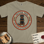 Praise Dog From Whom All Blessings Flow Rottweiler T-Shirt flat lay in Khaki, featuring a Roman mosaic ring medallion of a seated Rottweiler with natural ears and a full undocked tail, built from terracotta and mahogany tiles and flanked by laurel branches, with "Praise Dog From Whom All Blessings Flow" lettering.