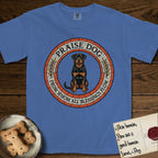 Praise Dog From Whom All Blessings Flow Rottweiler T-Shirt flat lay in Mystic Blue, featuring a Roman mosaic ring medallion of a seated Rottweiler with natural ears and a full undocked tail, built from terracotta and mahogany tiles and flanked by laurel branches, with "Praise Dog From Whom All Blessings Flow" lettering.