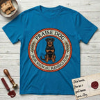 Praise Dog From Whom All Blessings Flow Rottweiler T-Shirt flat lay in Sapphire, featuring a Roman mosaic ring medallion of a seated Rottweiler with natural ears and a full undocked tail, built from terracotta and mahogany tiles and flanked by laurel branches, with "Praise Dog From Whom All Blessings Flow" lettering.