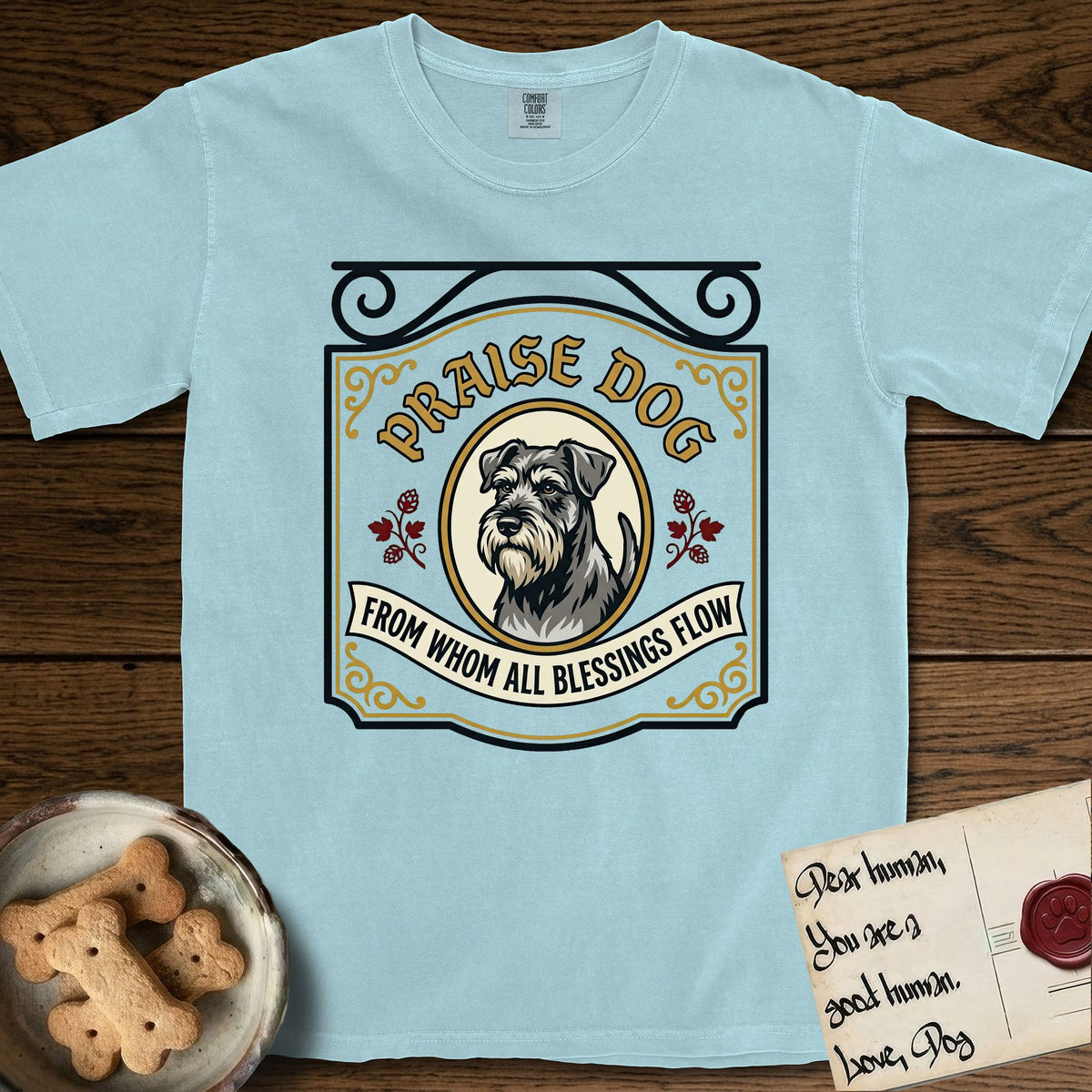 Praise Dog From Whom All Blessings Flow Schnauzer T-Shirt flat lay in Chambray, featuring a vintage tavern sign with a bearded Schnauzer portrait in a gilded oval, hops sprigs, and a ribbon banner, with the words Praise Dog From Whom All Blessings Flow.