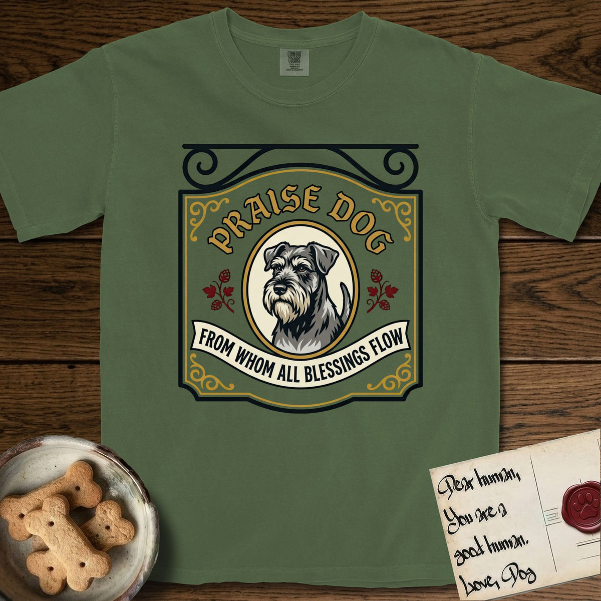 Praise Dog From Whom All Blessings Flow Schnauzer T-Shirt flat lay in Moss, featuring a vintage tavern sign with a bearded Schnauzer portrait in a gilded oval, hops sprigs, and a ribbon banner, with the words Praise Dog From Whom All Blessings Flow.