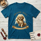 Praise Dog From Whom All Blessings Flow Shih Tzu T-Shirt flat lay in Antique Sapphire, featuring an old-master devotional oil painting of a Shih Tzu seated with one paw raised in blessing, a floating gold halo and streaming light, a shower of small gold blessings, and gilt "Praise Dog From Whom All Blessings Flow" lettering on a ribbon scroll.