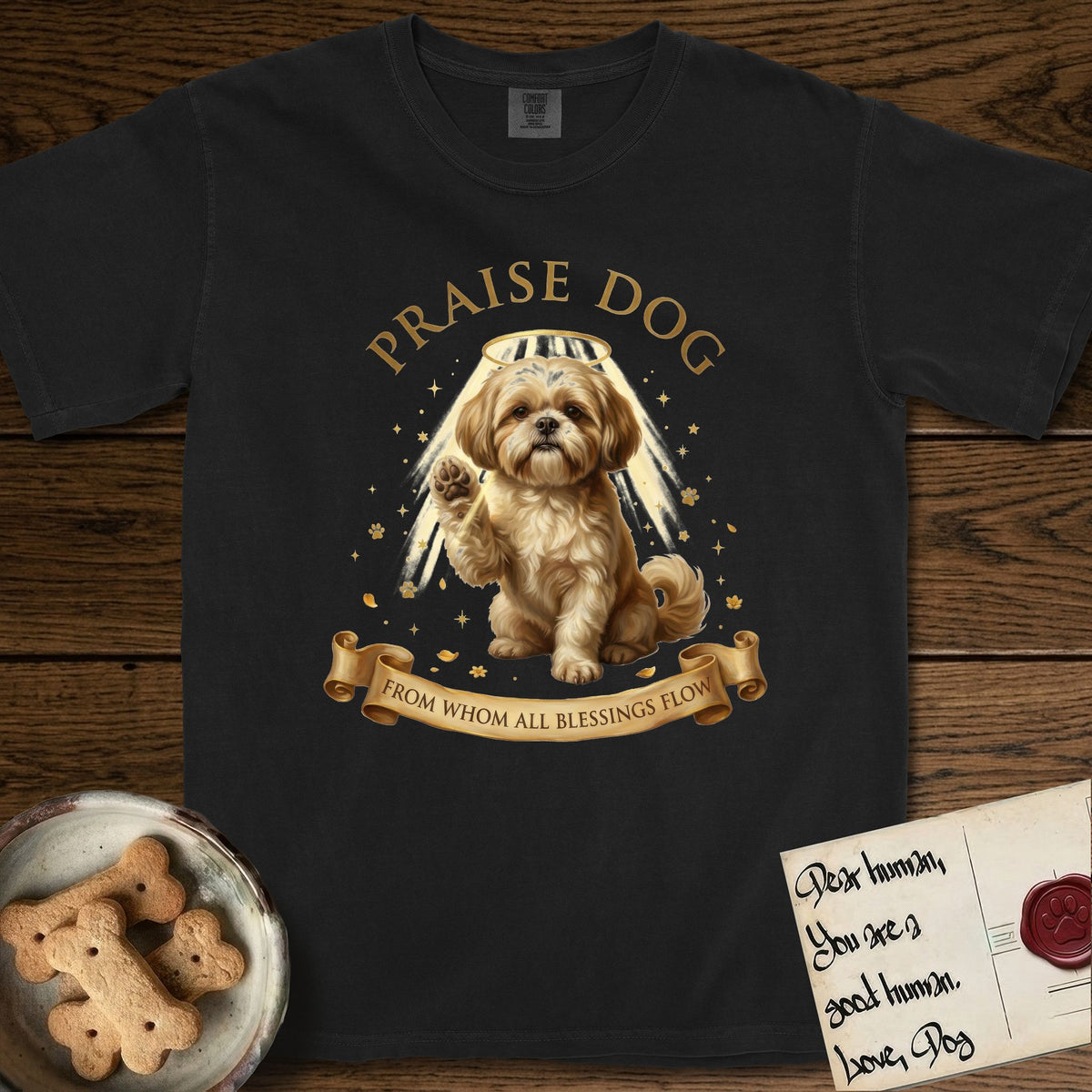 Praise Dog From Whom All Blessings Flow Shih Tzu T-Shirt flat lay in Black, featuring an old-master devotional oil painting of a Shih Tzu seated with one paw raised in blessing, a floating gold halo and streaming light, a shower of small gold blessings, and gilt "Praise Dog From Whom All Blessings Flow" lettering on a ribbon scroll.