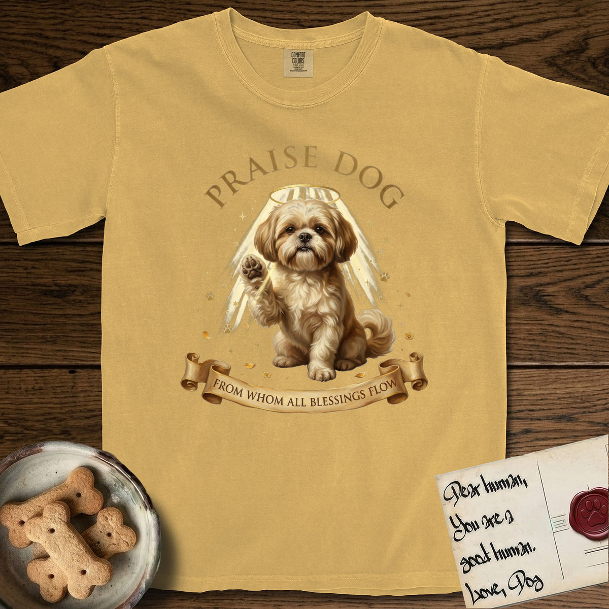 Praise Dog From Whom All Blessings Flow Shih Tzu T-Shirt flat lay in Mustard, featuring an old-master devotional oil painting of a Shih Tzu seated with one paw raised in blessing, a floating gold halo and streaming light, a shower of small gold blessings, and gilt "Praise Dog From Whom All Blessings Flow" lettering on a ribbon scroll.