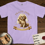Praise Dog From Whom All Blessings Flow Shih Tzu T-Shirt flat lay in Orchid, featuring an old-master devotional oil painting of a Shih Tzu seated with one paw raised in blessing, a floating gold halo and streaming light, a shower of small gold blessings, and gilt "Praise Dog From Whom All Blessings Flow" lettering on a ribbon scroll.