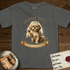 Praise Dog From Whom All Blessings Flow Shih Tzu T-Shirt flat lay in Pepper, featuring an old-master devotional oil painting of a Shih Tzu seated with one paw raised in blessing, a floating gold halo and streaming light, a shower of small gold blessings, and gilt "Praise Dog From Whom All Blessings Flow" lettering on a ribbon scroll.