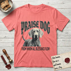 Praise Dog From Whom All Blessings Flow Weimaraner T-Shirt flat lay in Coral Silk, featuring a gothic halftone poster with a Weimaraner staring straight ahead beneath heavy blackletter lettering and the words Praise Dog From Whom All Blessings Flow.