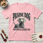 Praise Dog From Whom All Blessings Flow Weimaraner T-Shirt flat lay in Light Pink, featuring a gothic halftone poster with a Weimaraner staring straight ahead beneath heavy blackletter lettering and the words Praise Dog From Whom All Blessings Flow.