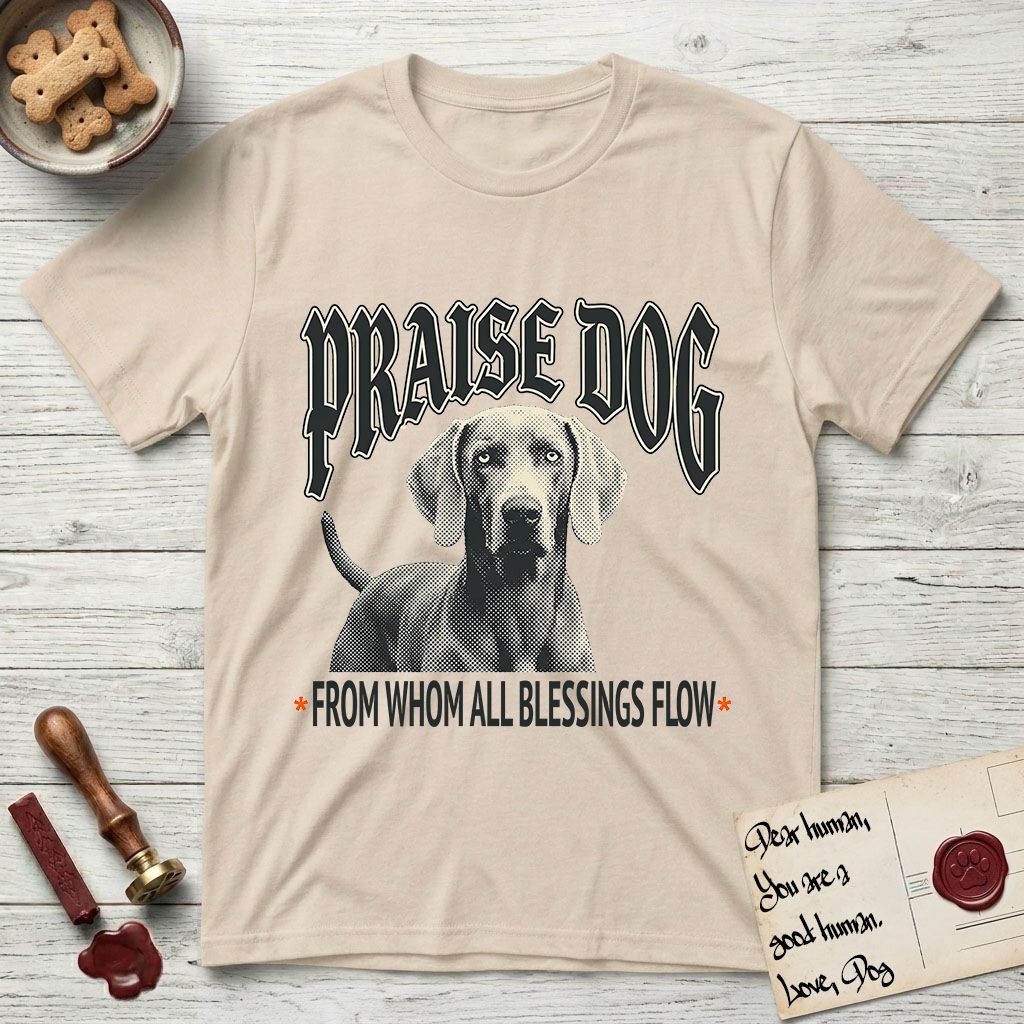 Praise Dog From Whom All Blessings Flow Weimaraner T-Shirt flat lay in Sand, featuring a gothic halftone poster with a Weimaraner staring straight ahead beneath heavy blackletter lettering and the words Praise Dog From Whom All Blessings Flow.