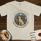 Praise Dog From Whom All Blessings Flow Yellow Lab T-Shirt flat lay in Ivory, featuring a warm vintage circular emblem with an upward-gazing Yellow Lab, a sunburst, and a devotional border of small hearts and stars.