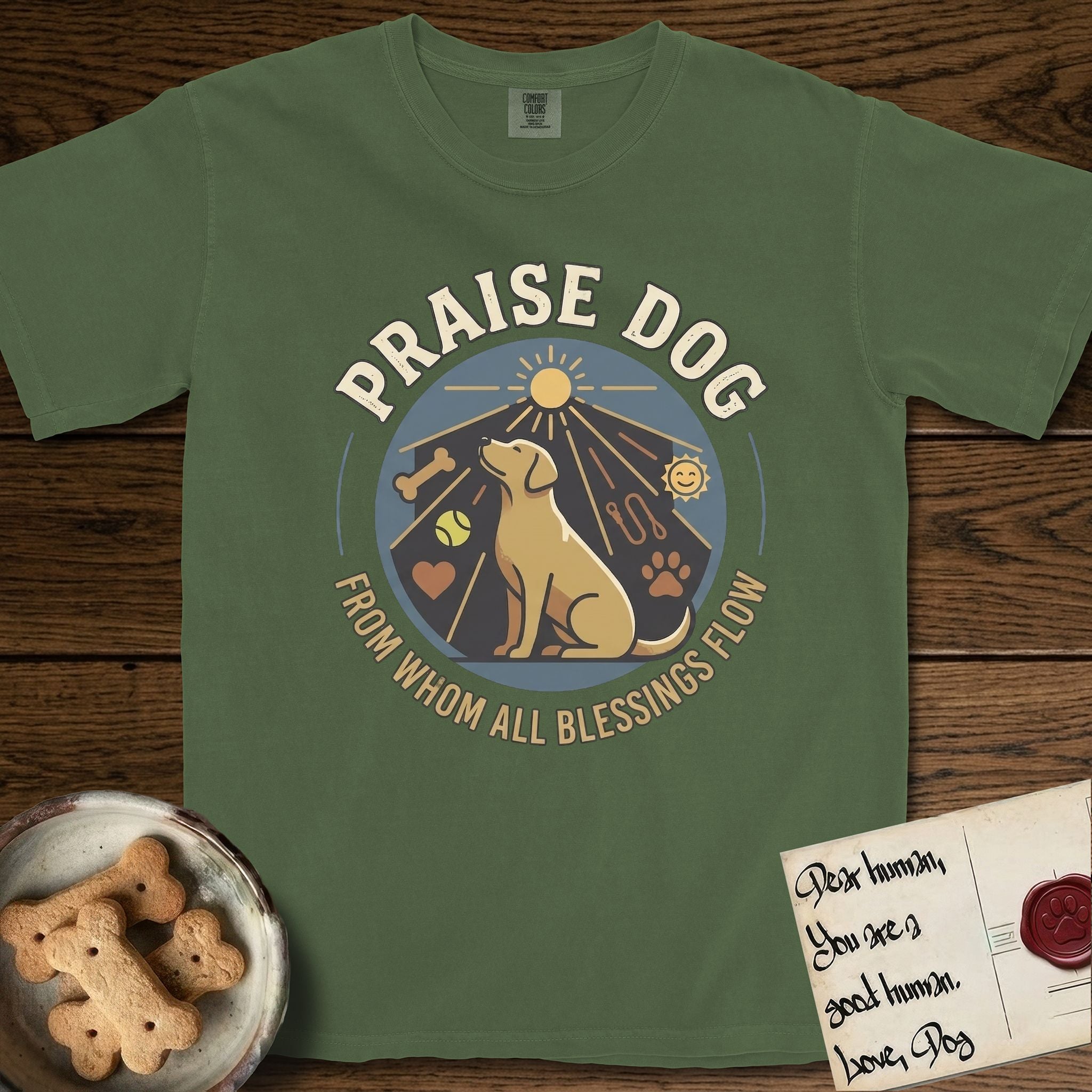 Praise Dog From Whom All Blessings Flow Yellow Lab T-Shirt flat lay in Moss, featuring a warm vintage circular emblem with an upward-gazing Yellow Lab, a sunburst, and a devotional border of small hearts and stars.