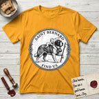 Patron Saint Medallion Saint Bernard T-Shirt flat lay in Gold, featuring a vintage engraving coin medallion of a haloed Saint Bernard carrying a child across a mountain pass, with the petition FIND US.