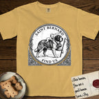 Patron Saint Medallion Saint Bernard T-Shirt flat lay in Mustard, featuring a vintage engraving coin medallion of a haloed Saint Bernard carrying a child across a mountain pass, with the petition FIND US.