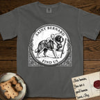 Patron Saint Medallion Saint Bernard T-Shirt flat lay in Pepper, featuring a vintage engraving coin medallion of a haloed Saint Bernard carrying a child across a mountain pass, with the petition FIND US.