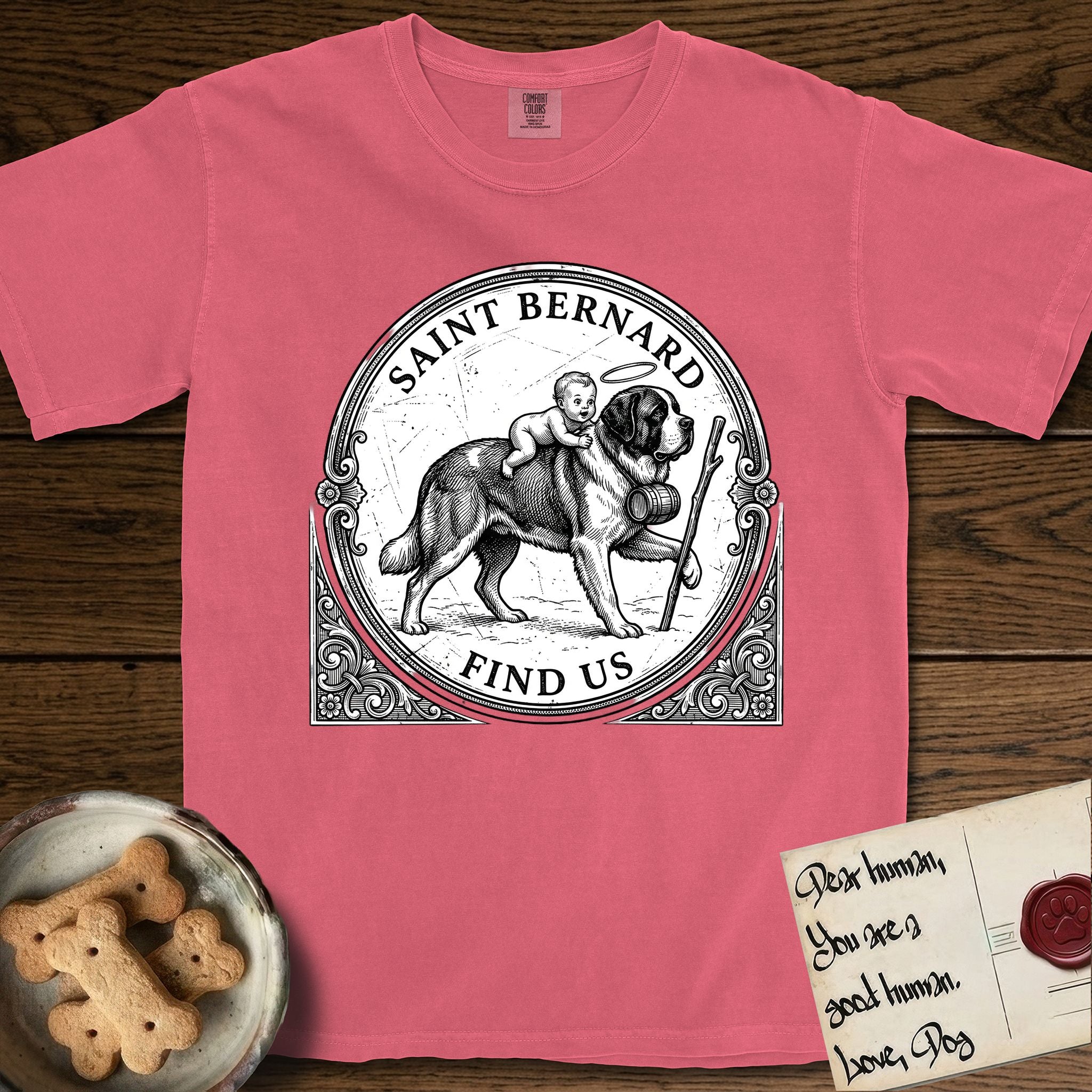 Patron Saint Medallion Saint Bernard T-Shirt flat lay in Watermelon, featuring a vintage engraving coin medallion of a haloed Saint Bernard carrying a child across a mountain pass, with the petition FIND US.