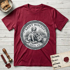 Patron Saint Medallion Saint Biscuit T-Shirt flat lay in Antique Cherry Red, featuring a vintage engraving coin medallion of a haloed Golden Retriever with a devotee resting against her and an open book, with the petition HEAL US.