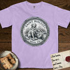 Patron Saint Medallion Saint Biscuit T-Shirt flat lay in Orchid, featuring a vintage engraving coin medallion of a haloed Golden Retriever with a devotee resting against her and an open book, with the petition HEAL US.
