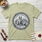 Patron Saint Medallion Saint Biscuit T-Shirt flat lay in Pistachio, featuring a vintage engraving coin medallion of a haloed Golden Retriever with a devotee resting against her and an open book, with the petition HEAL US.