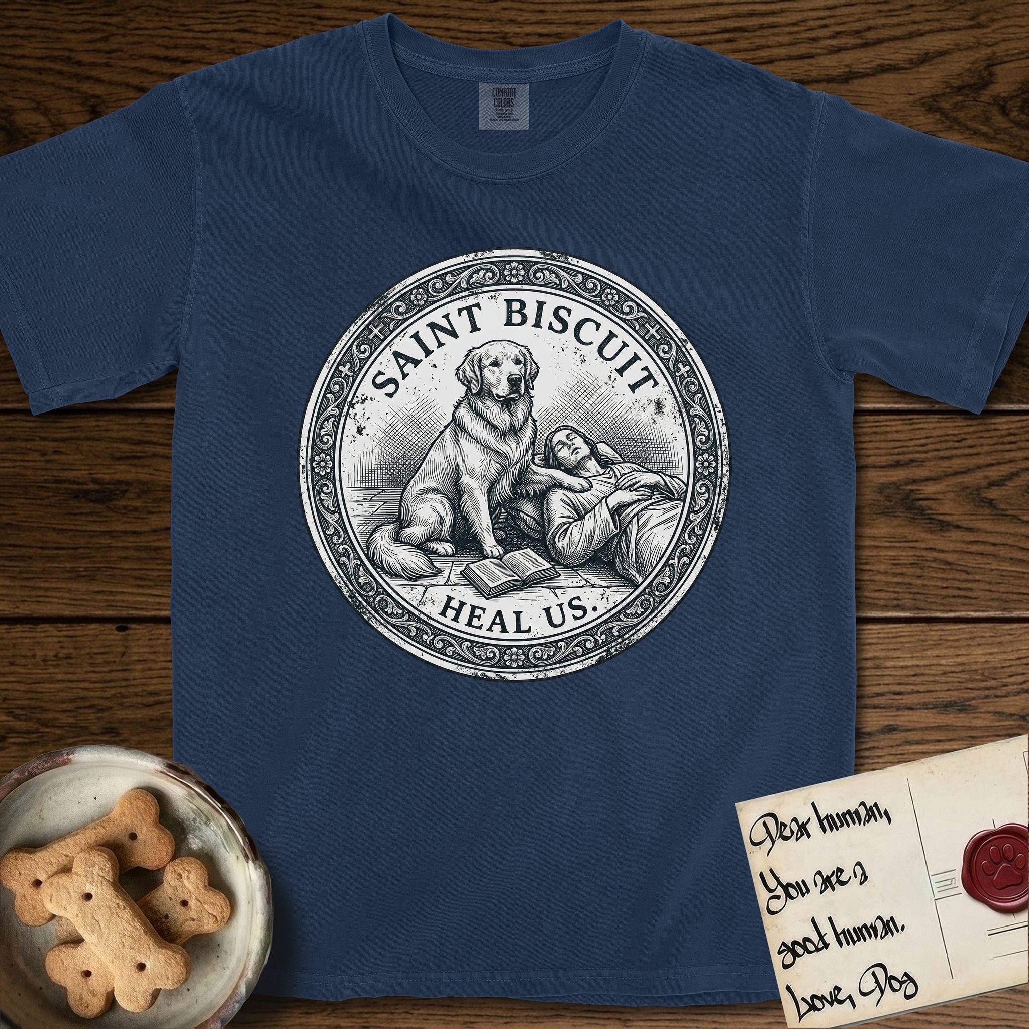 Patron Saint Medallion Saint Biscuit T-Shirt flat lay in True Navy, featuring a vintage engraving coin medallion of a haloed Golden Retriever with a devotee resting against her and an open book, with the petition HEAL US.