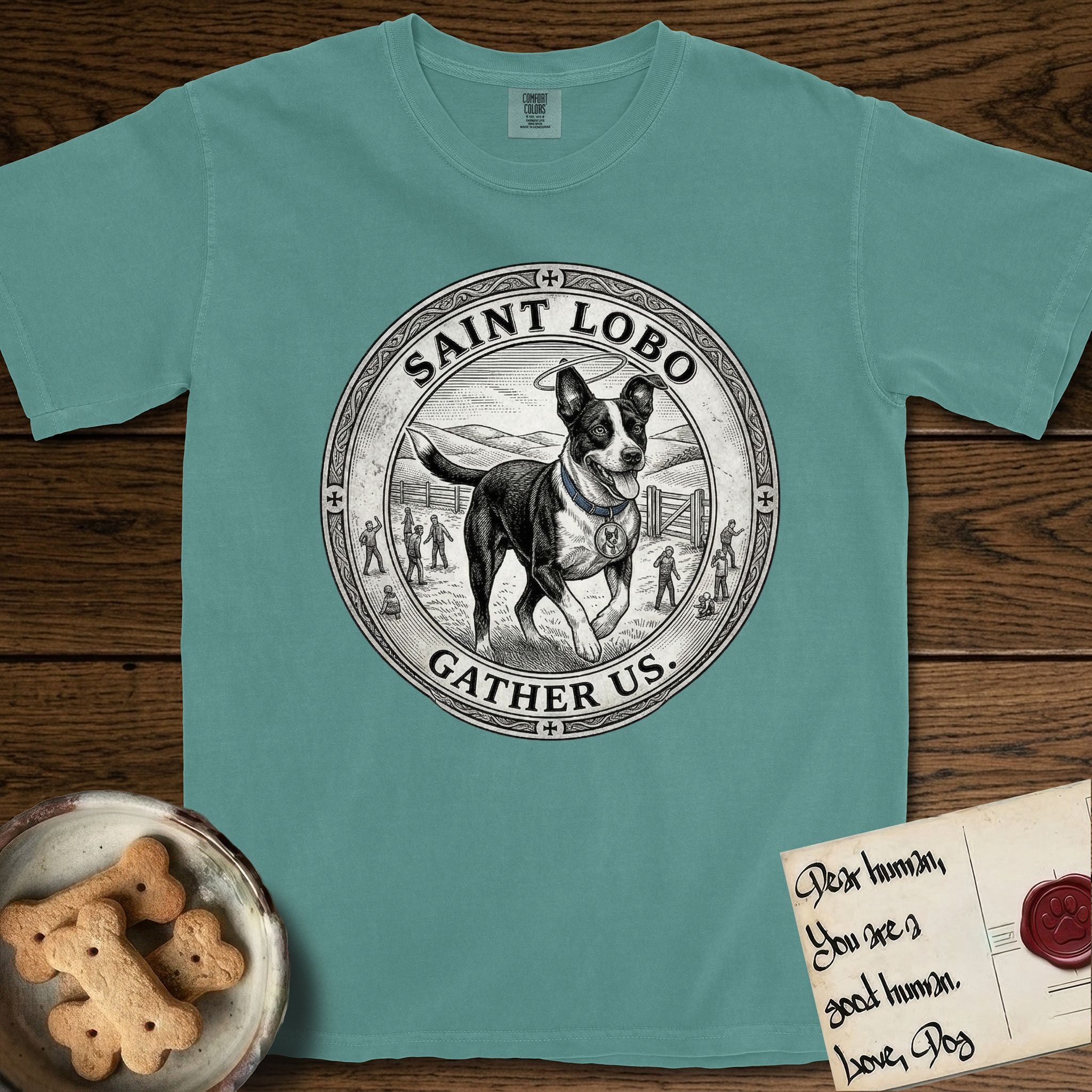 Patron Saint Medallion Saint Lobo T-Shirt flat lay in Blue Spruce, featuring a vintage engraving coin medallion of haloed Saint Lobo running across open ground, with the petition GATHER US.