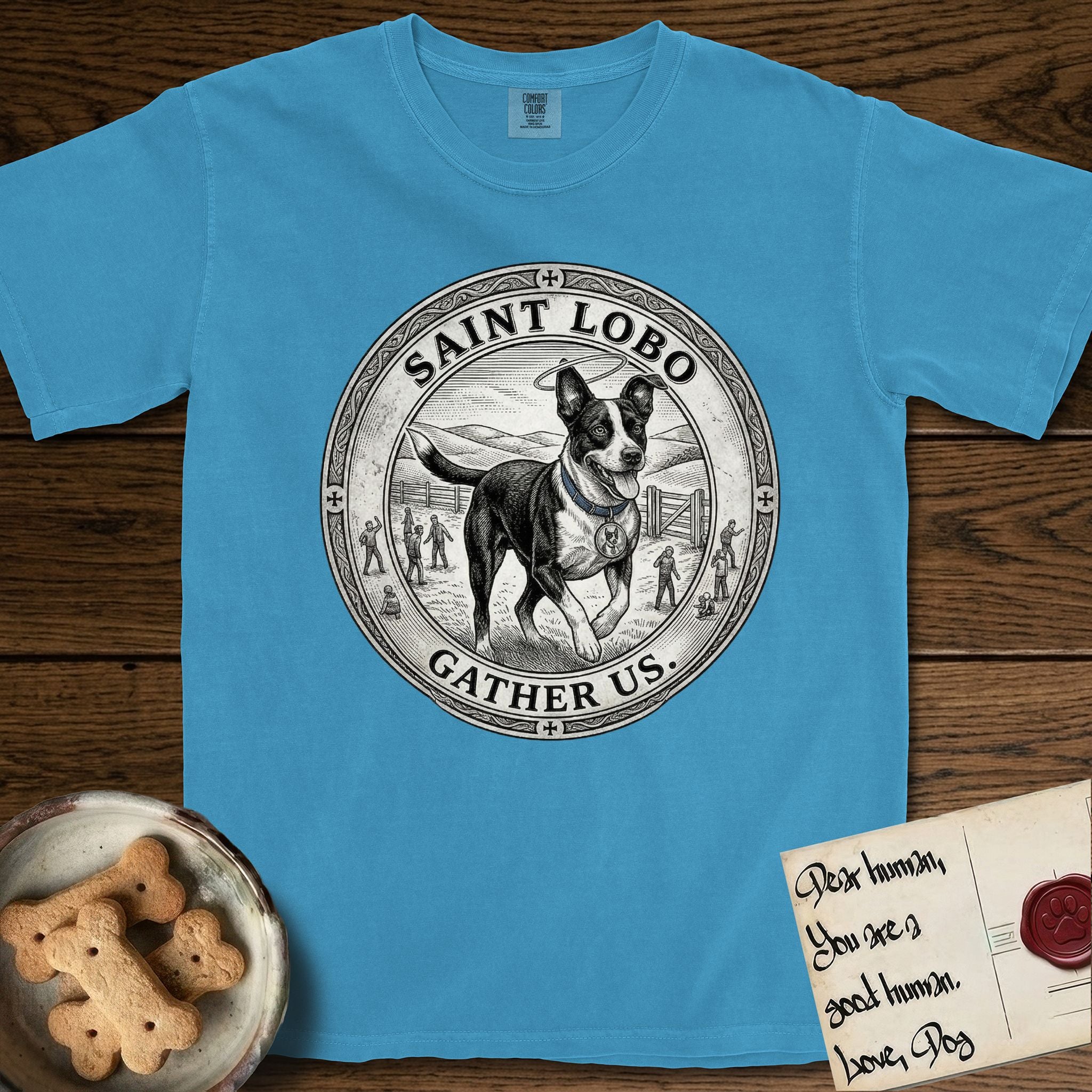 Patron Saint Medallion Saint Lobo T-Shirt flat lay in Royal Caribe, featuring a vintage engraving coin medallion of haloed Saint Lobo running across open ground, with the petition GATHER US.