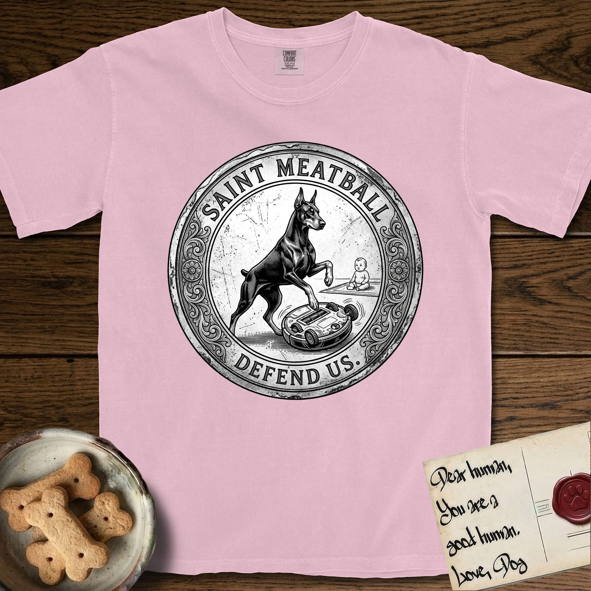 Patron Saint Medallion Saint Meatball T-Shirt flat lay in Blossom, featuring a vintage engraving coin medallion of a haloed Doberman rising on his hind legs, with the petition DEFEND US.
