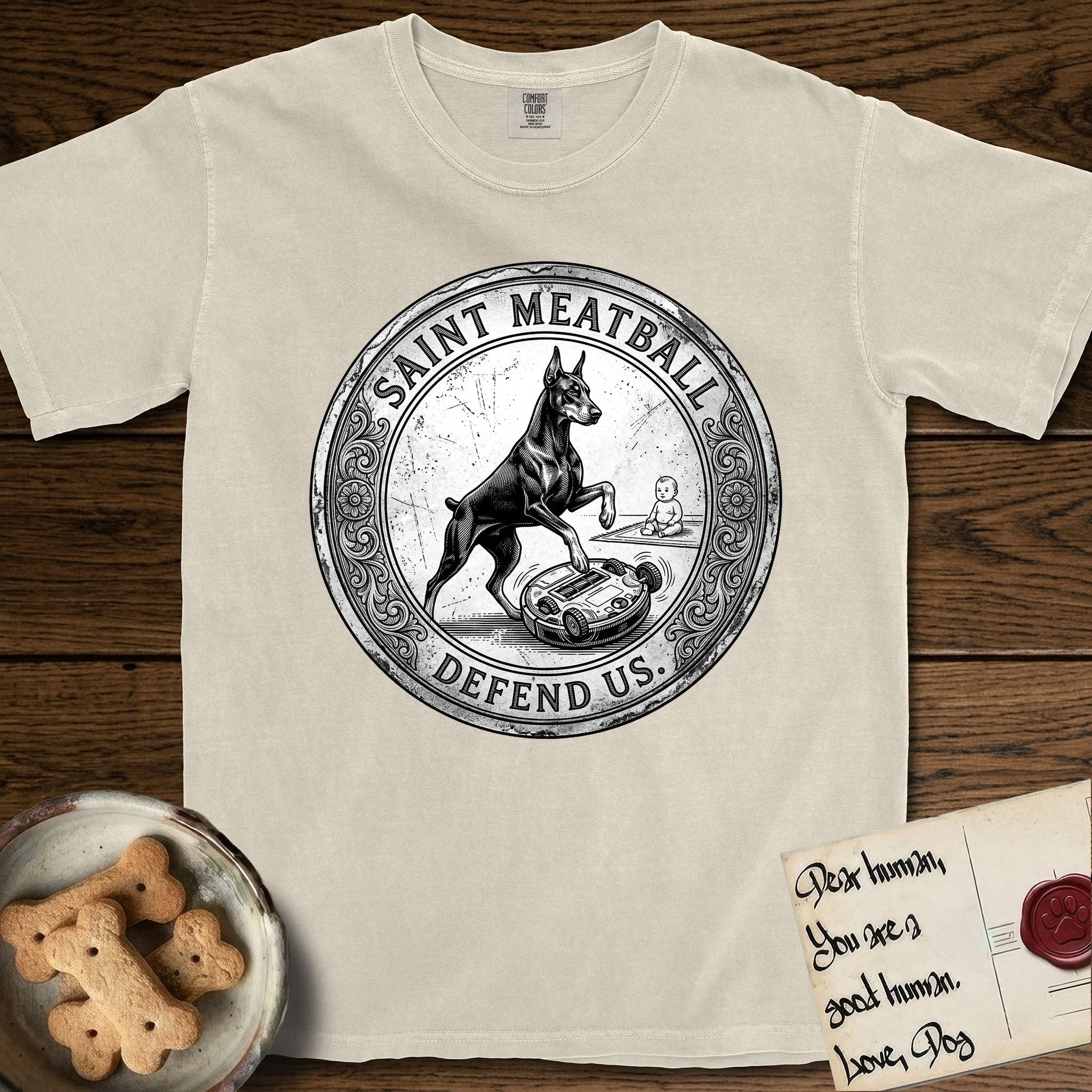 Patron Saint Medallion Saint Meatball T-Shirt flat lay in Ivory, featuring a vintage engraving coin medallion of a haloed Doberman rising on his hind legs, with the petition DEFEND US.