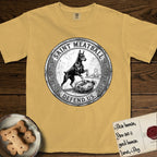 Patron Saint Medallion Saint Meatball T-Shirt flat lay in Mustard, featuring a vintage engraving coin medallion of a haloed Doberman rising on his hind legs, with the petition DEFEND US.