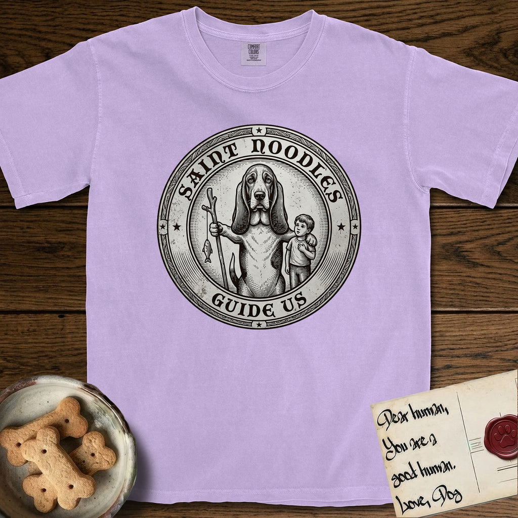 Patron Saint Medallion Saint Noodles T-Shirt flat lay in Orchid, featuring a vintage engraving coin medallion of a haloed Basset Hound with a staff and a child at her side, with the petition GUIDE US.