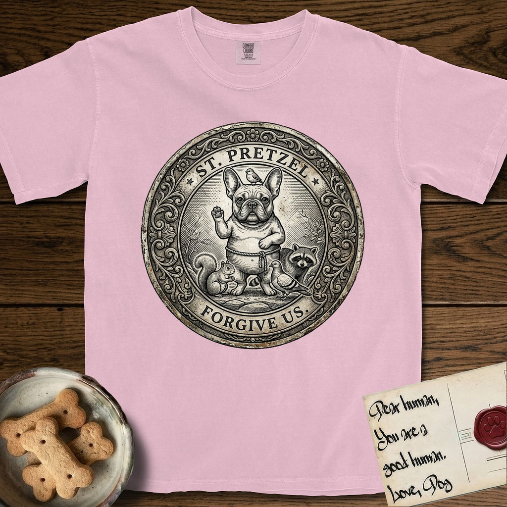 Patron Saint Medallion Saint Pretzel T-Shirt flat lay in Blossom, featuring an ornate vintage engraving coin medallion of a haloed French Bulldog raising one paw, a small bird on his head and woodland animals at his feet, with the petition FORGIVE US.
