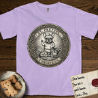 Patron Saint Medallion Saint Pretzel T-Shirt flat lay in Orchid, featuring an ornate vintage engraving coin medallion of a haloed French Bulldog raising one paw, a small bird on his head and woodland animals at his feet, with the petition FORGIVE US.