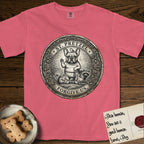 Patron Saint Medallion Saint Pretzel T-Shirt flat lay in Watermelon, featuring an ornate vintage engraving coin medallion of a haloed French Bulldog raising one paw, a small bird on his head and woodland animals at his feet, with the petition FORGIVE US.