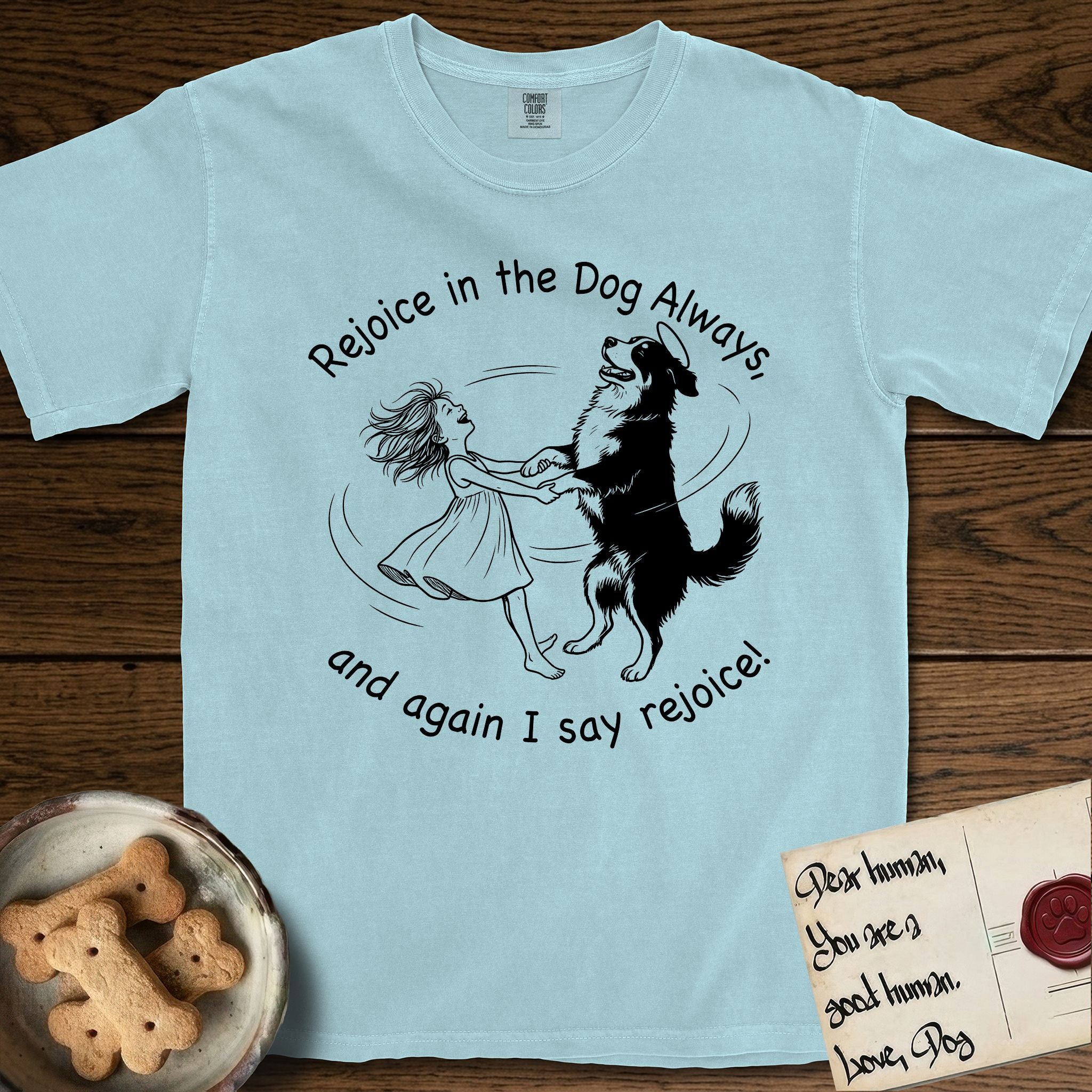 Rejoice in the Dog Bernese Mountain Dog T-Shirt flat lay in Chambray, featuring a sparse pen-and-ink illustration of a girl and her Bernese Mountain Dog spinning together, her feet lifting off the ground.