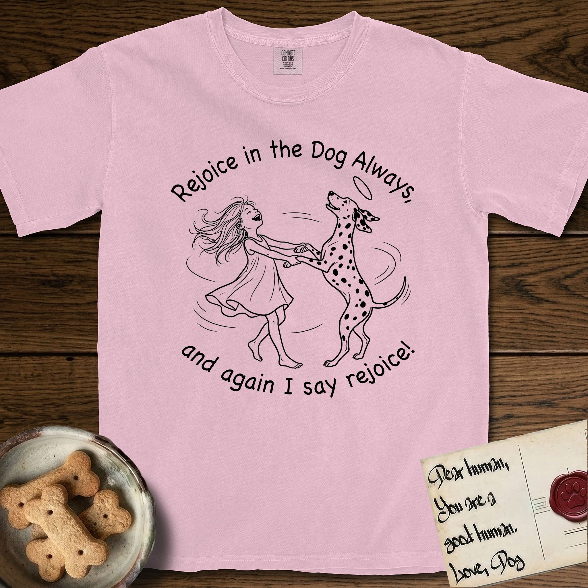 Rejoice in the Dog Dalmatian T-Shirt flat lay in Blossom, featuring a sparse pen-and-ink illustration of a girl and her Dalmatian spinning together, both heads thrown back in joy.