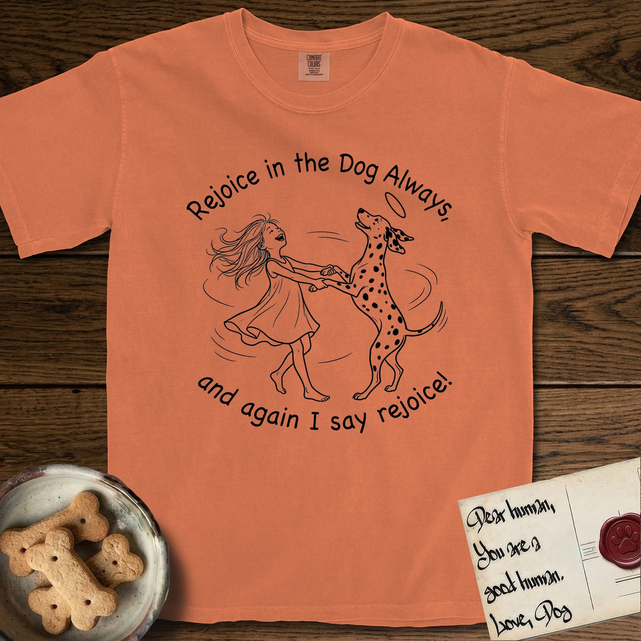 Rejoice in the Dog Dalmatian T-Shirt flat lay in Melon, featuring a sparse pen-and-ink illustration of a girl and her Dalmatian spinning together, both heads thrown back in joy.
