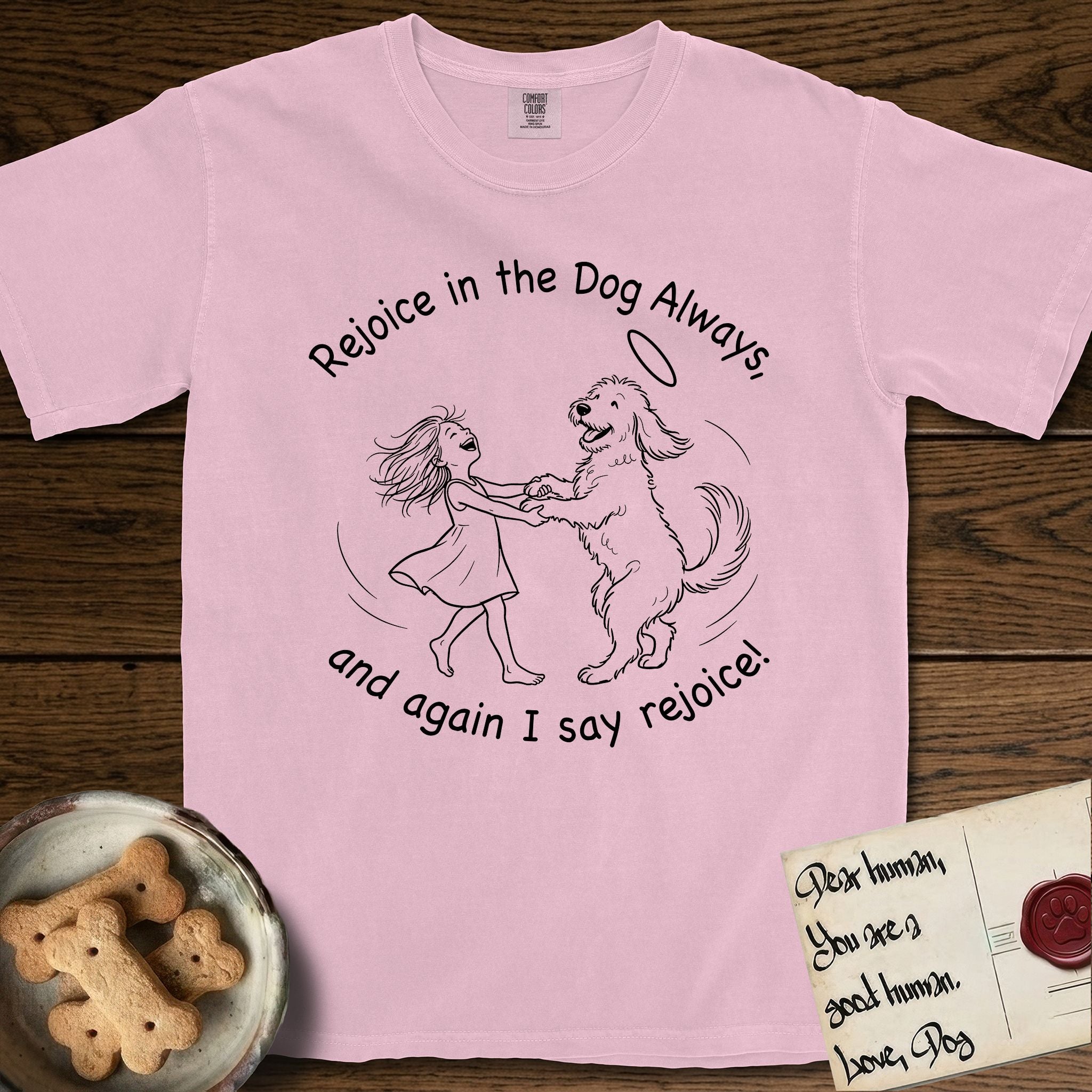 Rejoice in the Dog Goldendoodle T-Shirt flat lay in Blossom, featuring a sparse pen-and-ink illustration of a girl and her Goldendoodle dancing together, fur flying, both heads thrown back.