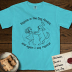 Rejoice in the Dog Goldendoodle T-Shirt flat lay in Lagoon Blue, featuring a sparse pen-and-ink illustration of a girl and her Goldendoodle dancing together, fur flying, both heads thrown back.