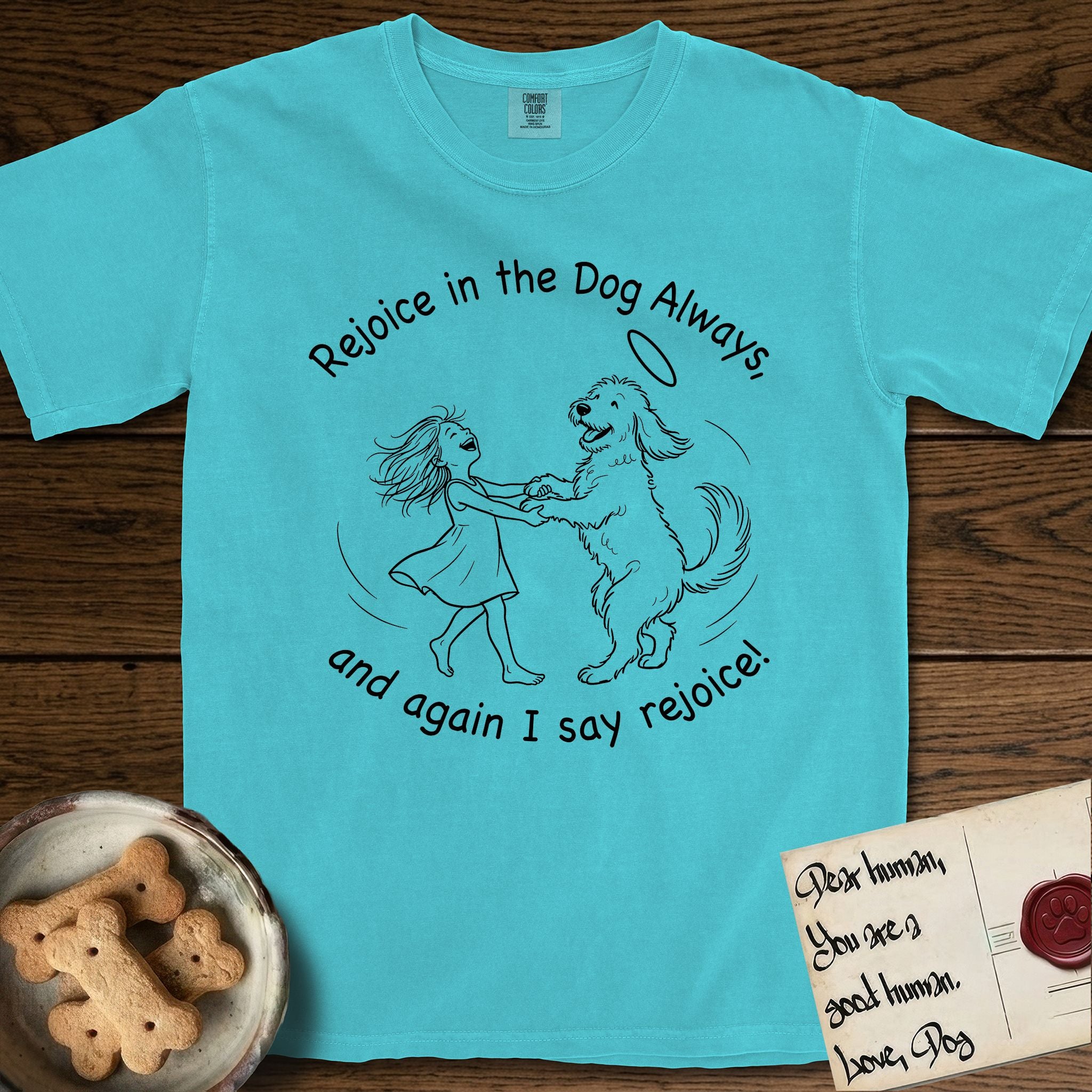 Rejoice in the Dog Goldendoodle T-Shirt flat lay in Lagoon Blue, featuring a sparse pen-and-ink illustration of a girl and her Goldendoodle dancing together, fur flying, both heads thrown back.