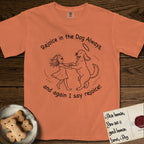 Rejoice in the Dog Goldendoodle T-Shirt flat lay in Melon, featuring a sparse pen-and-ink illustration of a girl and her Goldendoodle dancing together, fur flying, both heads thrown back.