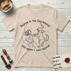 Rejoice in the Dog Goldendoodle T-Shirt flat lay in Sand, featuring a sparse pen-and-ink illustration of a girl and her Goldendoodle dancing together, fur flying, both heads thrown back.