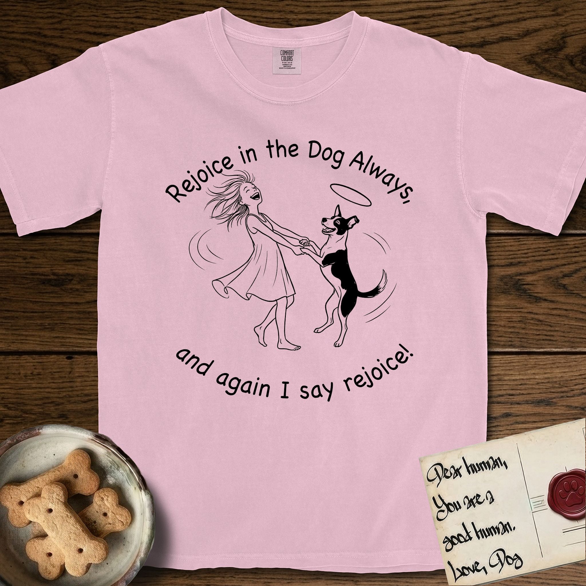 Rejoice in the Dog Lobo T-Shirt flat lay in Blossom, featuring a sparse pen-and-ink illustration of a girl and her haloed Dog Lobo spinning together, hands and paws clasped.