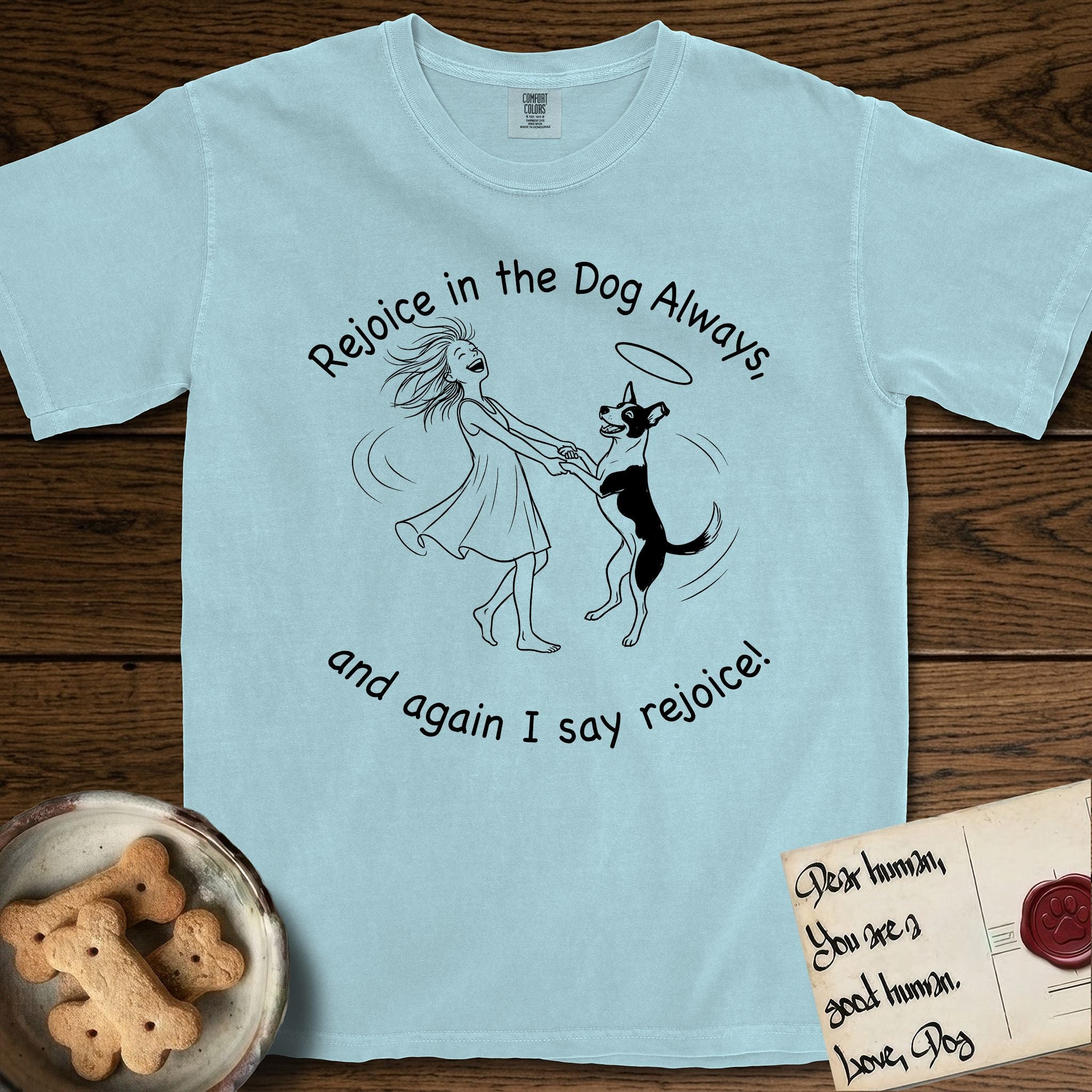 Rejoice in the Dog Lobo T-Shirt flat lay in Chambray, featuring a sparse pen-and-ink illustration of a girl and her haloed Dog Lobo spinning together, hands and paws clasped.